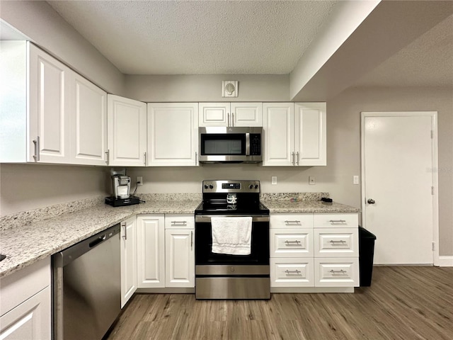 kitchen with stainless steel appliances, white cabinets, a textured ceiling, and light wood-type flooring