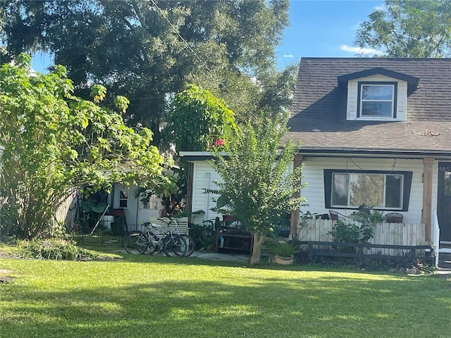 view of front facade with a shingled roof, fence, and a front yard