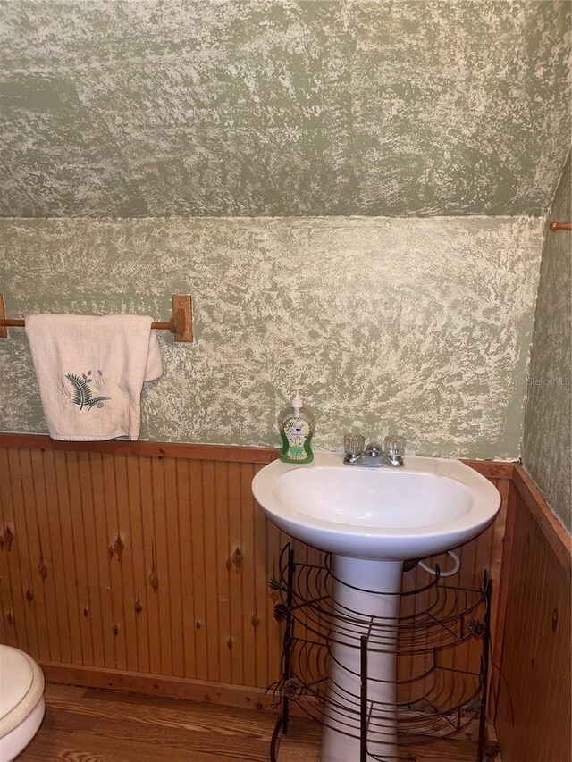 bathroom with wood-type flooring, wood walls, sink, and toilet