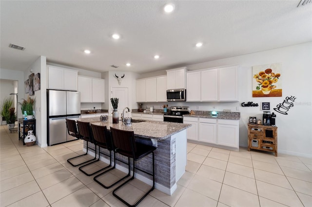 kitchen featuring appliances with stainless steel finishes, a kitchen island with sink, white cabinetry, and a breakfast bar