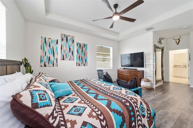 bedroom featuring ceiling fan, ensuite bathroom, a raised ceiling, and hardwood / wood-style floors