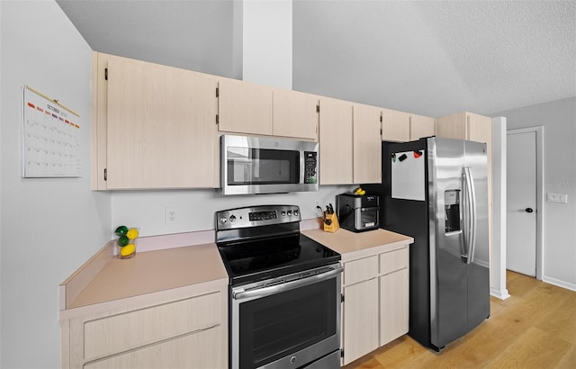 kitchen with a textured ceiling, light hardwood / wood-style floors, stainless steel appliances, and light brown cabinets