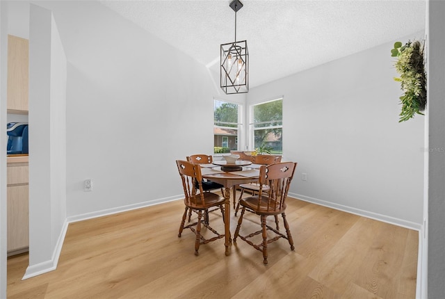 dining room with vaulted ceiling, a chandelier, light hardwood / wood-style floors, and a textured ceiling