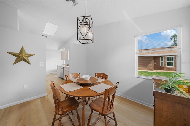 dining area featuring vaulted ceiling, light hardwood / wood-style flooring, a healthy amount of sunlight, and a notable chandelier