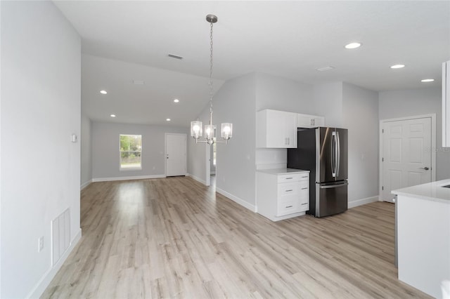 kitchen with white cabinets, light hardwood / wood-style floors, stainless steel fridge, decorative light fixtures, and vaulted ceiling