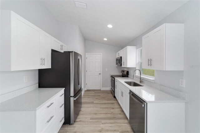 kitchen with light wood-type flooring, sink, white cabinetry, vaulted ceiling, and appliances with stainless steel finishes