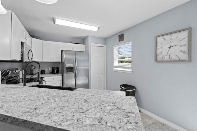 kitchen with appliances with stainless steel finishes, white cabinetry, kitchen peninsula, light tile patterned floors, and sink