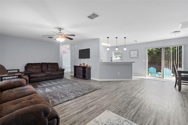 living room featuring a textured ceiling, ceiling fan, and light hardwood / wood-style flooring