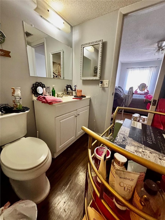 bathroom featuring vanity, a textured ceiling, toilet, ceiling fan, and hardwood / wood-style floors