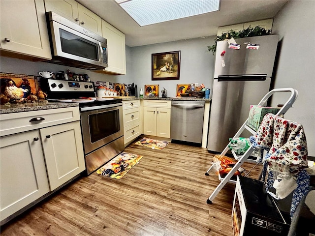 kitchen with appliances with stainless steel finishes, cream cabinetry, light hardwood / wood-style flooring, and a skylight