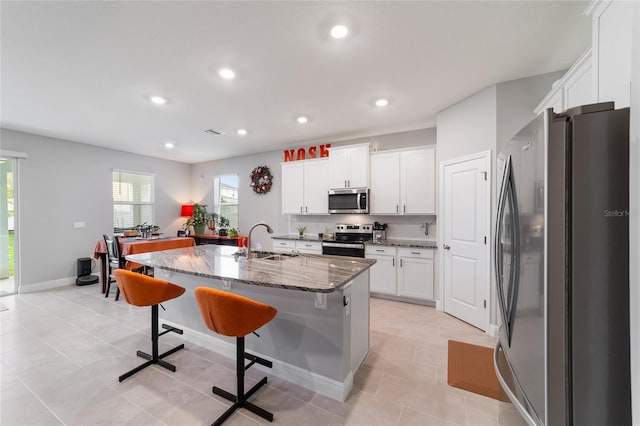 kitchen with dark stone counters, an island with sink, white cabinets, a kitchen breakfast bar, and stainless steel appliances