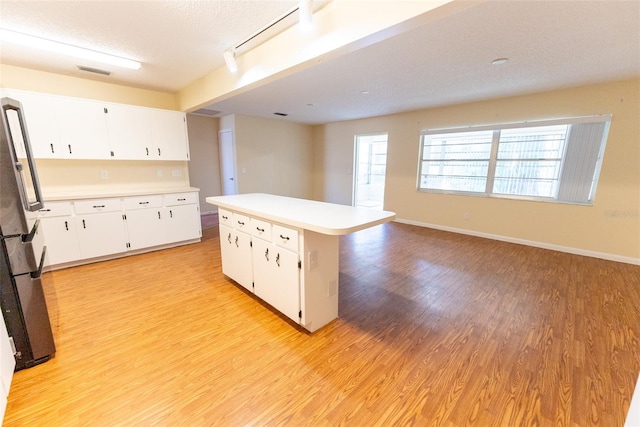 kitchen with stainless steel fridge, light wood-type flooring, white cabinetry, a kitchen island, and a textured ceiling