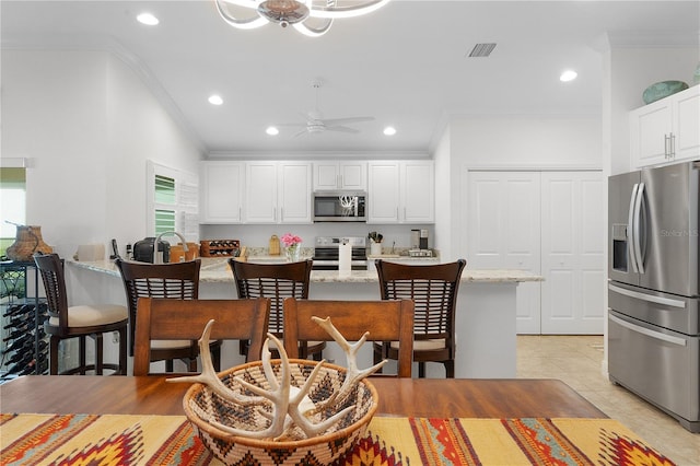 kitchen with crown molding, appliances with stainless steel finishes, light stone counters, and white cabinetry