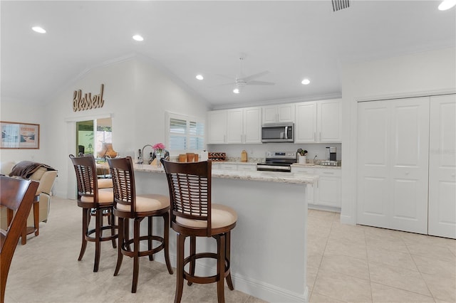 kitchen featuring lofted ceiling, a kitchen breakfast bar, white cabinets, and stainless steel appliances