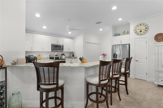 kitchen with kitchen peninsula, white cabinetry, stainless steel appliances, light stone counters, and a breakfast bar