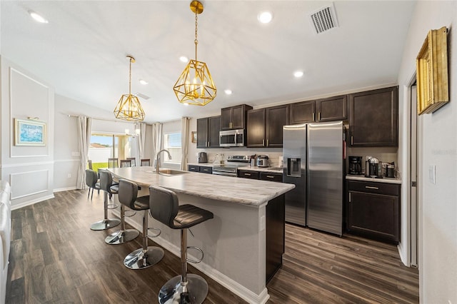 kitchen with a kitchen island with sink, stainless steel appliances, hanging light fixtures, and dark wood-type flooring