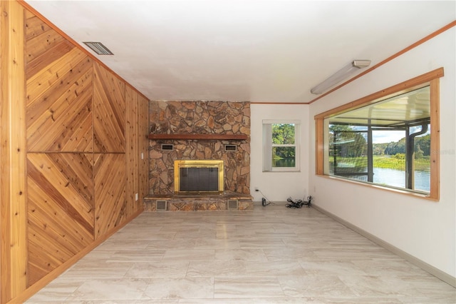 unfurnished living room with a stone fireplace, plenty of natural light, ornamental molding, and a water view