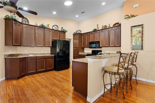 kitchen featuring light hardwood / wood-style floors, kitchen peninsula, black appliances, light stone countertops, and ceiling fan