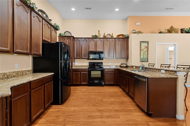 kitchen with light hardwood / wood-style floors, light stone counters, kitchen peninsula, black appliances, and sink