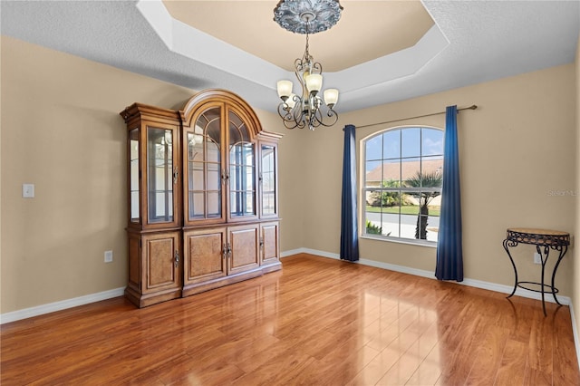 unfurnished dining area with a notable chandelier, a raised ceiling, hardwood / wood-style floors, and a textured ceiling