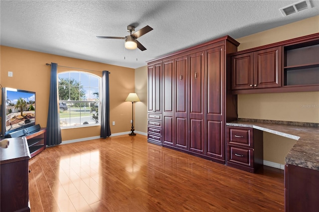 home office with a textured ceiling, ceiling fan, built in desk, and hardwood / wood-style flooring