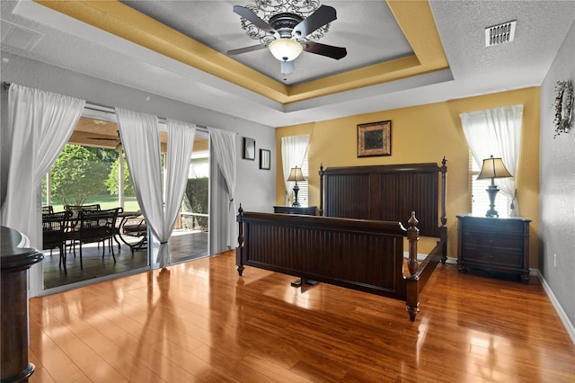 bedroom featuring wood-type flooring, a textured ceiling, a raised ceiling, and access to exterior