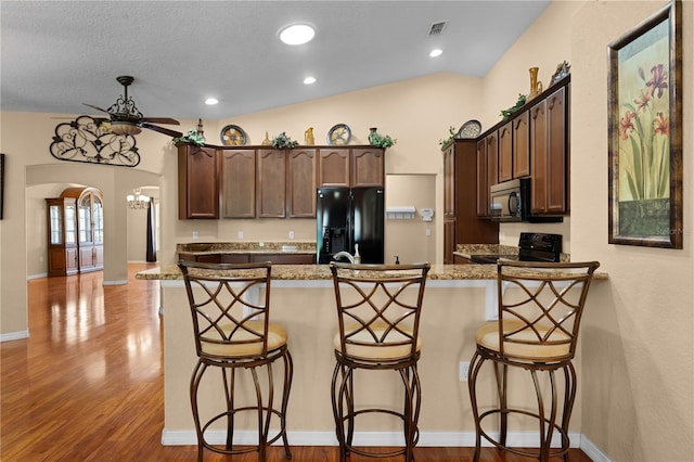 kitchen with lofted ceiling, light wood-type flooring, a kitchen breakfast bar, and black appliances