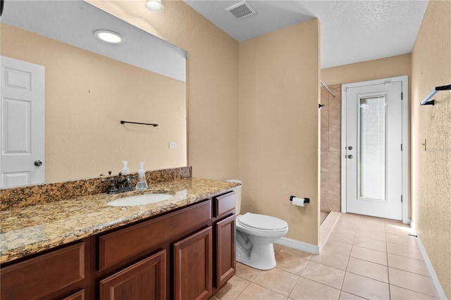 bathroom with vanity, tiled shower, a textured ceiling, tile patterned floors, and toilet