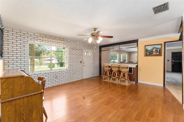 interior space featuring brick wall, a textured ceiling, wood-type flooring, and ceiling fan