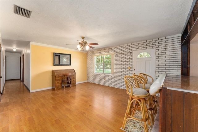 living room featuring a textured ceiling, light hardwood / wood-style flooring, crown molding, ceiling fan, and brick wall