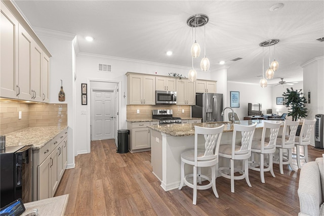 kitchen with appliances with stainless steel finishes, wood-type flooring, an island with sink, and decorative light fixtures