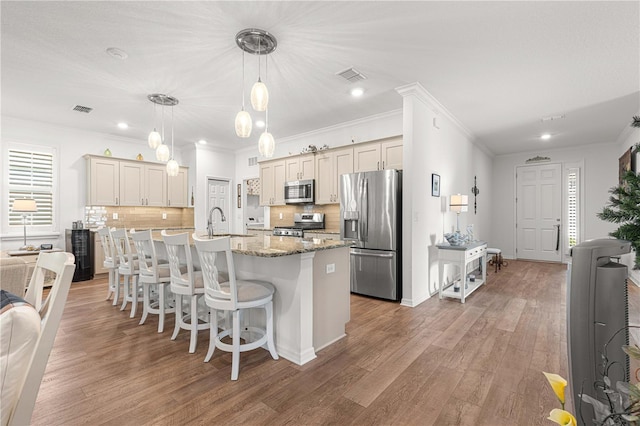 kitchen with hanging light fixtures, a center island with sink, backsplash, appliances with stainless steel finishes, and dark hardwood / wood-style floors