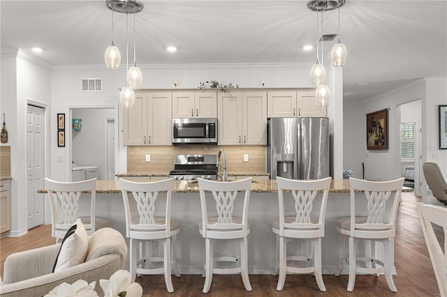 kitchen featuring dark hardwood / wood-style floors, a kitchen island with sink, stainless steel appliances, decorative light fixtures, and light stone countertops