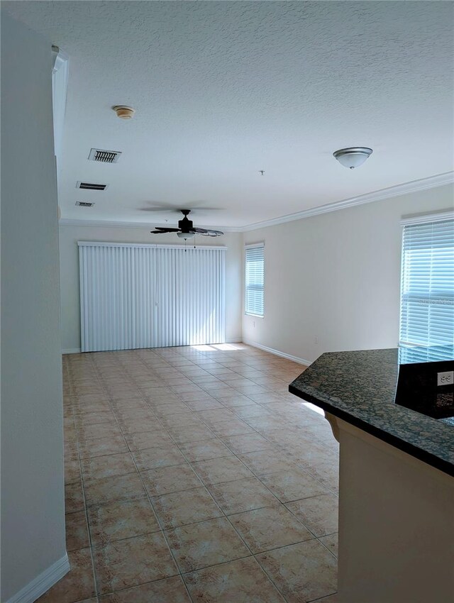 unfurnished living room with ornamental molding, a textured ceiling, light tile patterned floors, and ceiling fan