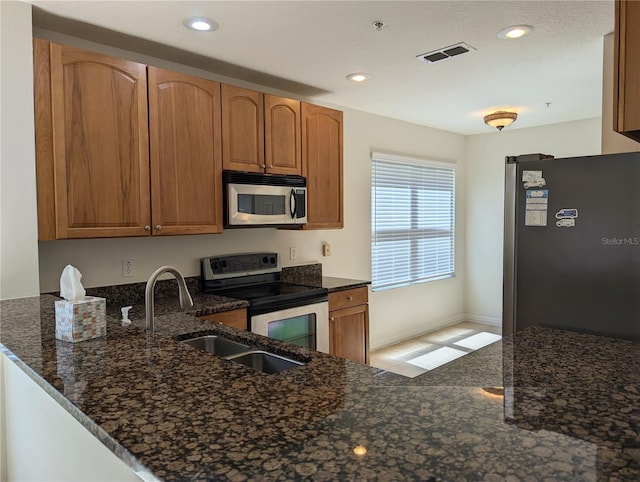 kitchen featuring sink, kitchen peninsula, stainless steel appliances, and dark stone countertops