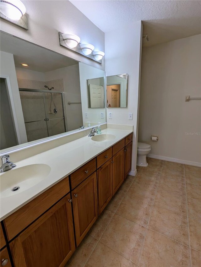 bathroom with a textured ceiling, toilet, vanity, an enclosed shower, and tile patterned flooring