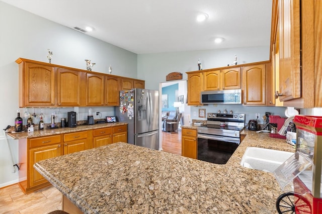 kitchen featuring light hardwood / wood-style flooring, light stone countertops, lofted ceiling, kitchen peninsula, and appliances with stainless steel finishes