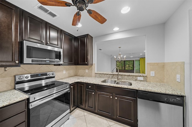 kitchen featuring appliances with stainless steel finishes, light stone counters, light tile patterned floors, dark brown cabinetry, and sink