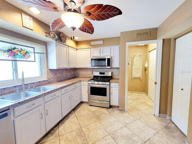 kitchen featuring ceiling fan, decorative backsplash, stainless steel appliances, white cabinets, and sink