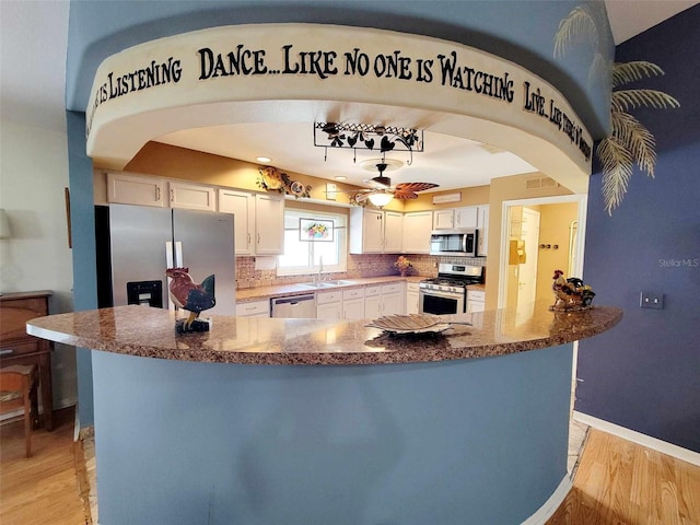 kitchen with white cabinets, stainless steel appliances, light wood-type flooring, and tasteful backsplash