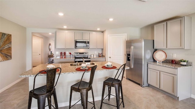 kitchen with appliances with stainless steel finishes, gray cabinetry, a kitchen bar, and a kitchen island with sink