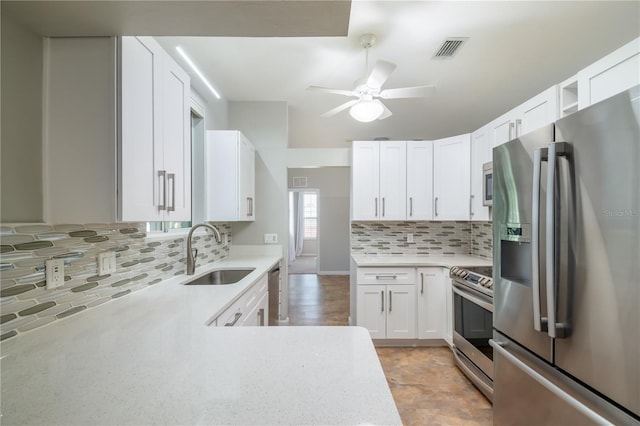 kitchen with tasteful backsplash, sink, white cabinetry, stainless steel appliances, and ceiling fan