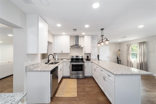 kitchen with sink, kitchen peninsula, wall chimney exhaust hood, appliances with stainless steel finishes, and decorative light fixtures