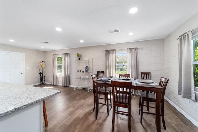 dining area with brick wall and dark wood-type flooring