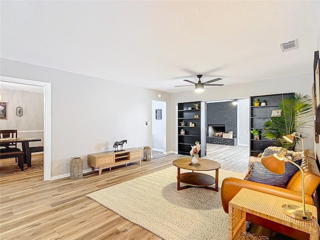 living room featuring hardwood / wood-style floors, a brick fireplace, and ceiling fan