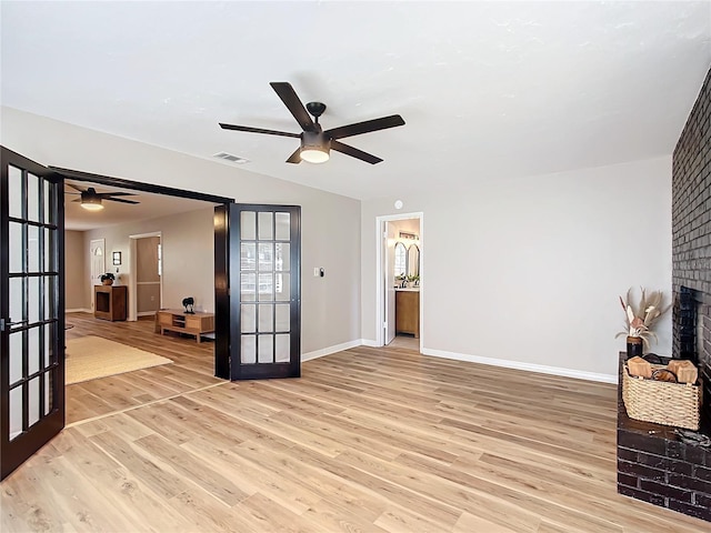 living room with a brick fireplace, light hardwood / wood-style flooring, ceiling fan, and french doors