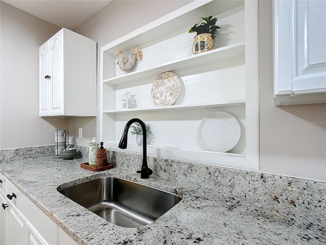 room details with light stone counters, sink, and white cabinets