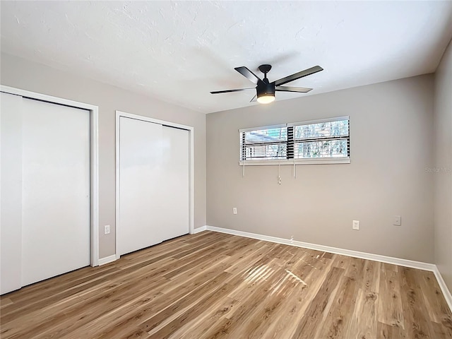 unfurnished bedroom with multiple closets, hardwood / wood-style floors, and ceiling fan