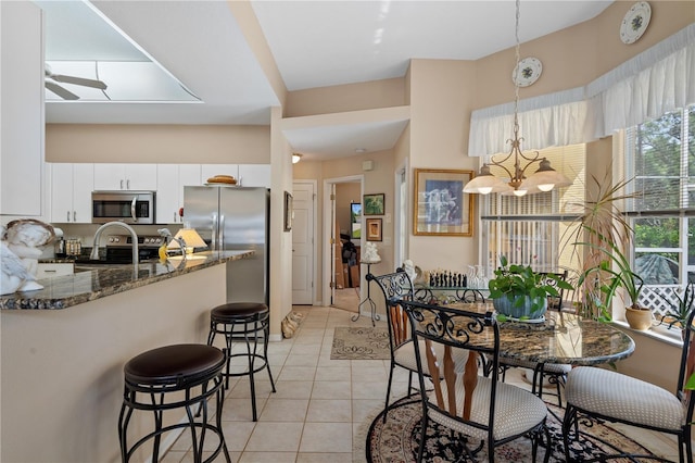 kitchen featuring appliances with stainless steel finishes, ceiling fan with notable chandelier, hanging light fixtures, white cabinets, and dark stone countertops