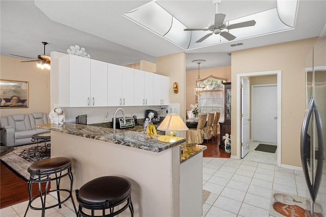 kitchen with kitchen peninsula, white cabinets, a kitchen bar, dark stone counters, and pendant lighting